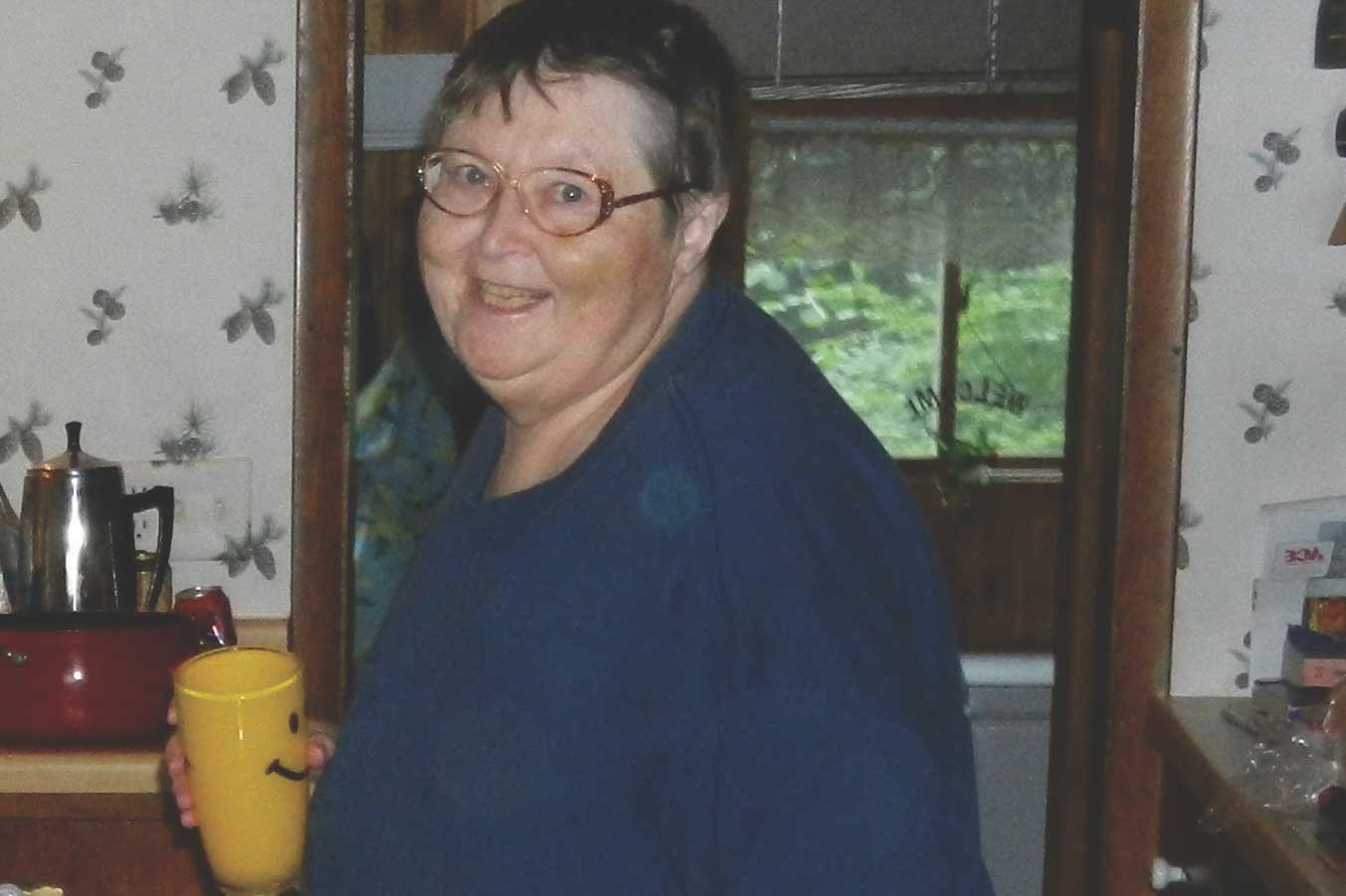 Donor Mary Ann Podal standing in her house holding a smiley face coffee mug