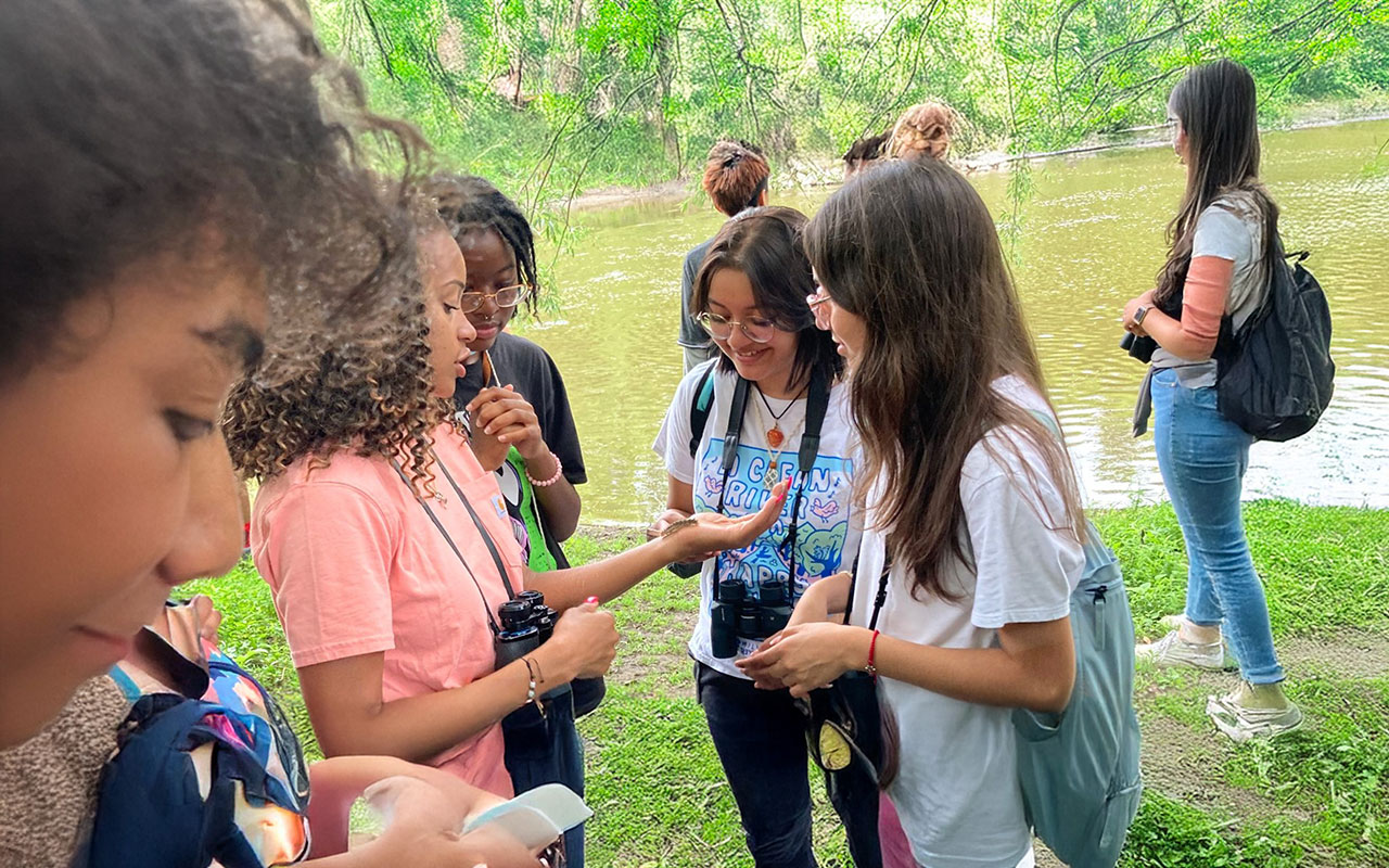 Youth participants stand by a river, observing nature together during a hands-on environmental education program.
